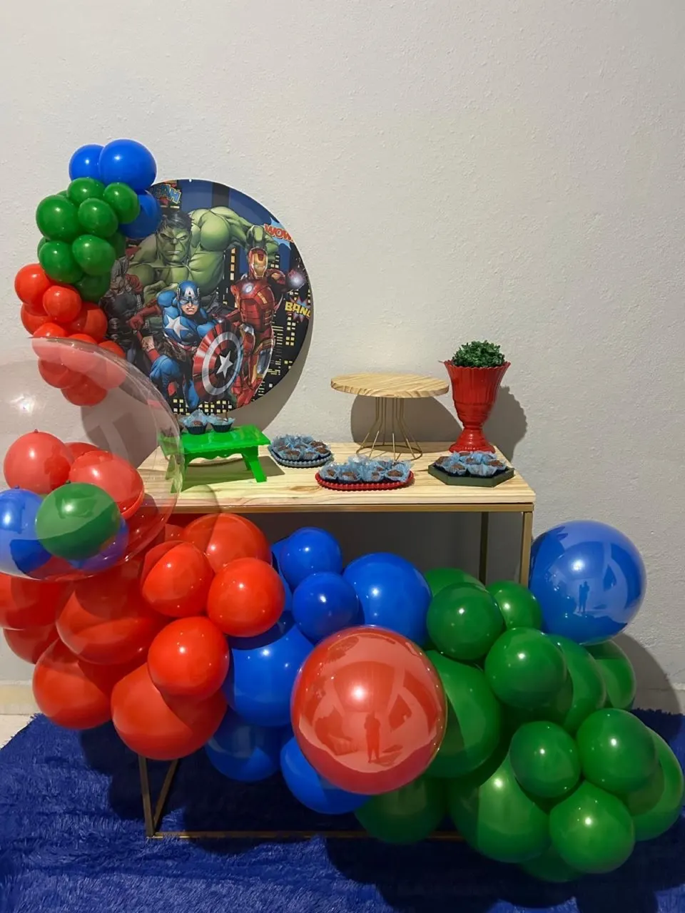 Kit Festa na Mesa Completo com tema dos Vingadores: mesa de madeira, painel redondo, arco de balões vermelhos, azuis e verdes, suportes de doce e jarro